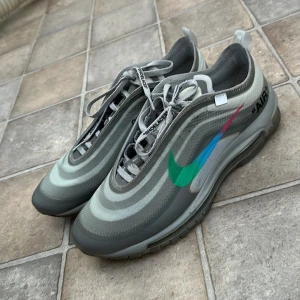 Nike Air Max 97 x Off-White - Säljer ett par Nike Air Max 97 i samarbete med Off-White. Skorna är gråa med ikoniska Off-White detaljer, text på snörena och en färgglad swoosh i grönt, blått och rött. Synlig Air Max-sula och Off-White logga på innersulan. De är precis som orginalet.