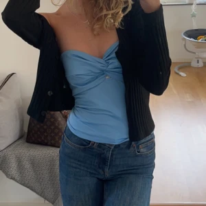 Ljusblå tubtopp med twistad detalj - Säljer en ljusblå tubtopp med snygg twistad detalj framtill. Toppen är axelbandslös och har en tight passform, perfekt att styla med jeans eller kjol.
