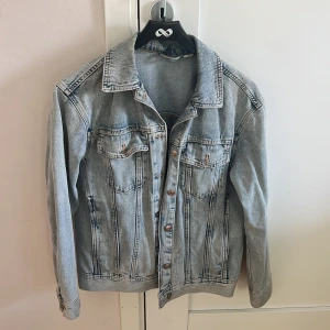 Ljusblå jeansjacka i klassisk modell - Säljer en ljusblå jeansjacka i klassisk modell med knappar framtill och två bröstfickor. Jackan har normal passform och långa ärmar.
