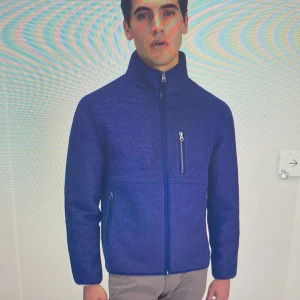 Mörkblå fleecejacka med dragkedja - Säljer en mörkblå fleecejacka från John Henric i ullmaterial. Jackan har hög krage, hel dragkedja framtill och tre fickor med dragkedja. Enkel och stilren design som passar till många tillfällen. Defekt på högra ficka då den fickan inte kan dras upp eller ner. Nypris 1499kr