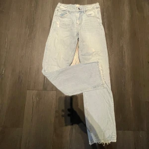 Ljusblå raka jeans  - Ljusblå jeans med rak passform och råa, fransiga benslut. Jeansen har ganska hög midja, lite slitningar och klassisk femficksmodell med knapp- och dragkedjegylf. Jeansen har en avslappnad look och är perfekta för en trendig vardagsstil.