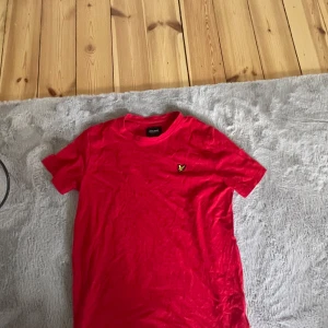 Röd t-shirt från Lyle & Scott Junior - Säljer en röd t-shirt från Lyle & Scott Junior med klassisk passform och korta ärmar. T-shirten har en liten broderad logga på bröstet och är tillverkad i mjuk bomull. Perfekt för en avslappnad stil.