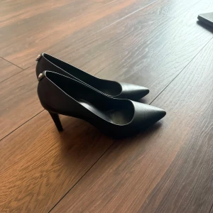 Svarta pumps från Michael Kors - Stilrena svarta pumps från Michael Kors med spetsig tå och klassisk klack. Skorna är i skinn och har en elegant form som passar perfekt till många olika outfits. Väldigt bra skick 