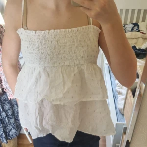 Vit volangig linnetopp från Gina Tricot - Säljer en söt vit linnetopp från Gina Tricot med smock upptill och dubbla volanger. Toppen har tunna axelband som går att plocka av och små diskreta prickar i tyget. Perfekt för varma dagar och enkel att matcha med jeans eller kjol. Har användit några gånger men i nyskick.  Frakt ingår inte. Säljer för att jag har växt ur dem. Har aldrig använts. 