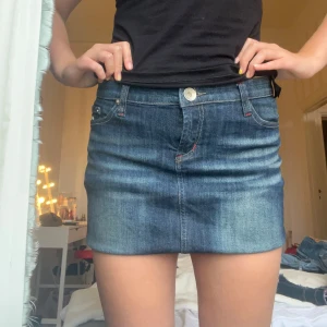 Mörkblå jeanskjol  - Säljer en klassisk mörkblå jeanskjol från Sixty, T&M jeans med femficksdesign och knappstängning framtill. Kjolen har snygga slitningar och kontrastsömmar, samt broderad logga bak. Perfekt till vardags med en t-shirt eller hoodie.