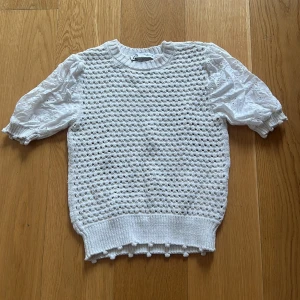 Vit stickad topp med spetsärmar från Zara - Superfin vit topp från Zara med stickad, hålig framsida och puffiga spetsärmar med broderade detaljer. Rund halsringning och ribbad nederkant med små bollar. Perfekt för vår och sommar! Nypris 399kr