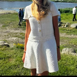studentklänning/ festklänning - Supersöt vit kortklänning med korta ärmar och markerad midja. Klänningen har dekorativa guldknappar framtill och ett diskret rutmönster i tyget. Perfekt för somriga tillfällen och har en klassisk, chic känsla. Jag hade den på studenten och fick massvis utav komplimanger och frågor om vart den är ifrån, slutsåld.