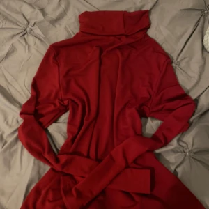 Röd långärmad med polokrage - Säljer en röd långärmad med hög polokrage och matchande bälte i midjan. Tröjan har en elegant och enkel design som passar perfekt till höst och vinter.