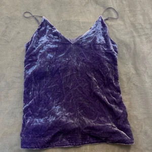 Lila sammetslinne med smala axelband - Säljer ett lila linne i mjuk sammet med smala axelband och v-ringning. Perfekt för att addera lite lyxig känsla till din outfit. Linnet har en lätt glansig yta och är riktigt skönt att bära.