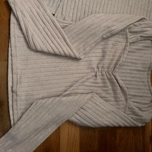 Ljusbeige ribbad långärmad tröja - Säljer en ljusbeige ribbad tröja med långa ärmar och lätt rynkdetalj vid bysten. Mjuk och stretchig, perfekt till vardags. Snygg och enkel att matcha med olika outfits.