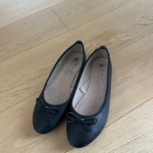 Svarta ballerinaskor med rosett - Säljer ett par klassiska svarta ballerinaskor.  Skorna har en liten rosett framtill och rund tå. Perfekta att matcha med både jeans och klänning. Snygg och enkel design som passar till mycket.