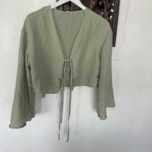 Ljusgrön croppad kofta från SHEIN - Säljer en ljusgrön croppad kofta från SHEIN i 100% polyester. Koftan har långa ärmar och knytning framtill, perfekt för lager-på-lager och en chill look.