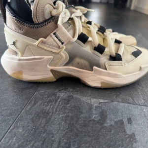 Jordan Why Not Zer0.3 sneakers i beige och svart - Säljer ett par Jordan Why Not Zer0.3 sneakers i beige och svart med coola detaljer och transparent mesh på sidorna. Skorna har snörning, platt sula och rund tå. Perfekta för dig som gillar basketinspirerad stil och unika sneakers.