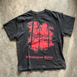 Svart band-tshirt med Mumincunt tryck - Cool svart t-shirt med stort rött Mumincunt tryck fram och bak. Framsidan har bandlogga och texten 'Offerskogens Hjarta', baksidan har en röd kanin med kedjor och texten 'Corrupting the Minds Of Innocent Souls'. Perfekt för dig som gillar alternativ stil.