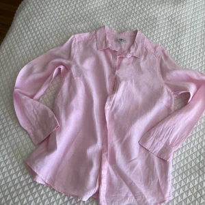 Ljusrosa linneskjorta från Hampton Republic - Säljer en ljusrosa skjorta i 100% linne. Skjortan har klassisk krage, långa ärmar och knäppning framtill. Perfekt för en avslappnad men ändå stilren look.