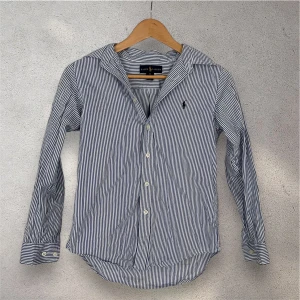 Polo Ralph Lauren Skjorta - Ralph Lauren skjorta i utmärkt skick! Den är i storlek 14 år, detta motsvarar ungefär 164 cm. Den är i riktigt fint skick och är i en najs design. Skjortan är köpt för 1 585 kronor. Vid eventuella frågor eller funderingar är det bara att hojta till! 