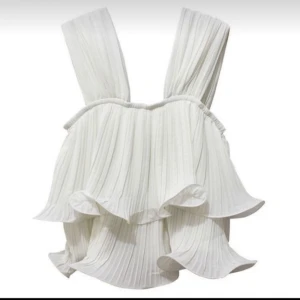 Vit volangtopp - Säljer en vit plisserad topp med breda axelband och volangdetaljer. Toppen har en luftig och flowy känsla, perfekt för varma dagar. 😊💗