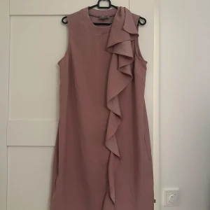 Rosa ärmlös klänning med volangdetalj - Snygg rosa ärmlös klänning från Esprit med en elegant volangdetalj framtill. Perfekt för en stilren look. Klänningen har en enkel och klassisk design som passar många tillfällen.