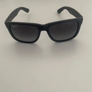 Rayband Justin  - Snygga svarta solglasögon från Ray-Ban med polariserade linser. Klassisk design med en stilren look. Perfekta för soliga dagar och ger ett bra skydd mot solen. Köpta på Zalando för 2200. Säljer för 600. Det finns en repa på de men den syns knappt 