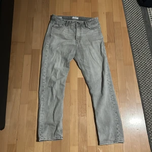 Grå jeans från Jack & Jones - Säljer ett par grå jeans från Jack & Jones med en loose fit. De har en klassisk femficksdesign och är perfekta för en avslappnad stil. Passar bra till både sneakers och kängor. Längd 32, midja 30