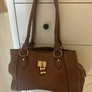 Brun axelväska med hänglåsdetalj - Snygg brun axelväska i skinn med en unik hänglåsdetalj framtill