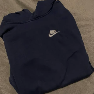 Mörkblå hoodie från Nike - Säljer en stilren mörkblå hoodie från Nike med deras ikoniska logga på bröstet. Perfekt för en avslappnad look. Passar bra till både träning och vardag.