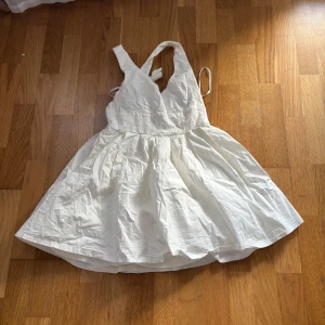 Vit klänning från Xenia - Säljer en söt vit klänning från Xenia med v-ringad design och korsade axelband. Klänningen har en luftig kjol och är perfekt för varma dagar. Den är tillverkad i ett lätt material som ger en skön känsla. Passar perfekt för sommarens alla tillfällen! 🌸