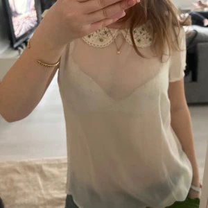 Vit blus med spetskrage - Säljer en söt vit blus med korta ärmar och en vacker spetskrage. Blusen är genomskinlig och har en feminin och elegant stil. Perfekt för en stilren look.💓
