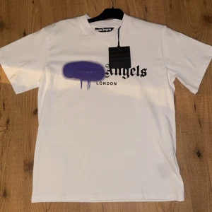 Vit t-shirt från Palm Angels - ‼️aldrig använd‼️Säljer en vit t-shirt från Palm Angels med en cool lila sprayfärgseffekt och texten 'London' under. Perfekt för en avslappnad stil med en twist. Kortärmad och i mjukt material.