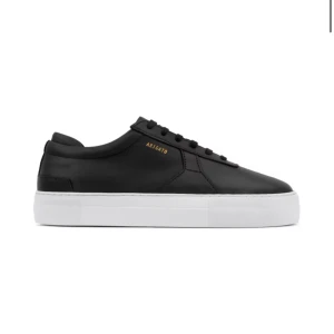 Svarta sneakers från Axel Arigato - Stilrena svarta sneakers i skinn från Axel Arigato med vit sula och diskret guldfärgad logga på sidan. Perfekta för en minimalistisk look.