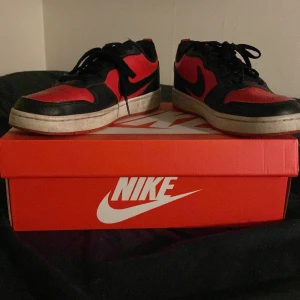 Nike sneakers i rött och svart - Snygga Nike sneakers i rött och svart med klassisk snörning. Skorna har en rund tå och en vit sula som ger en cool kontrast. Perfekta för en sportig look eller vardagsstil.