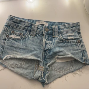 Blå lågmidjade jeansshorts från Pull&Bear - Säljer ett par snygga blå jeansshorts i storlek 32 från Pull&Bear. De har en lågmidjad passform med slitna detaljer och fransar vid benen. Perfekta för en avslappnad sommarlook. Shortsen har fem fickor och knappar bak. Skitsnygga men säljer pga de är för små för mig.