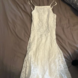 Vit spetsklänning från FB Sister - Säljer en vacker vit spetsklänning från FB Sister i storlek XS. Klänningen har smala axelband och en öppen rygg med knytning. Perfekt för sommarens festligheter!