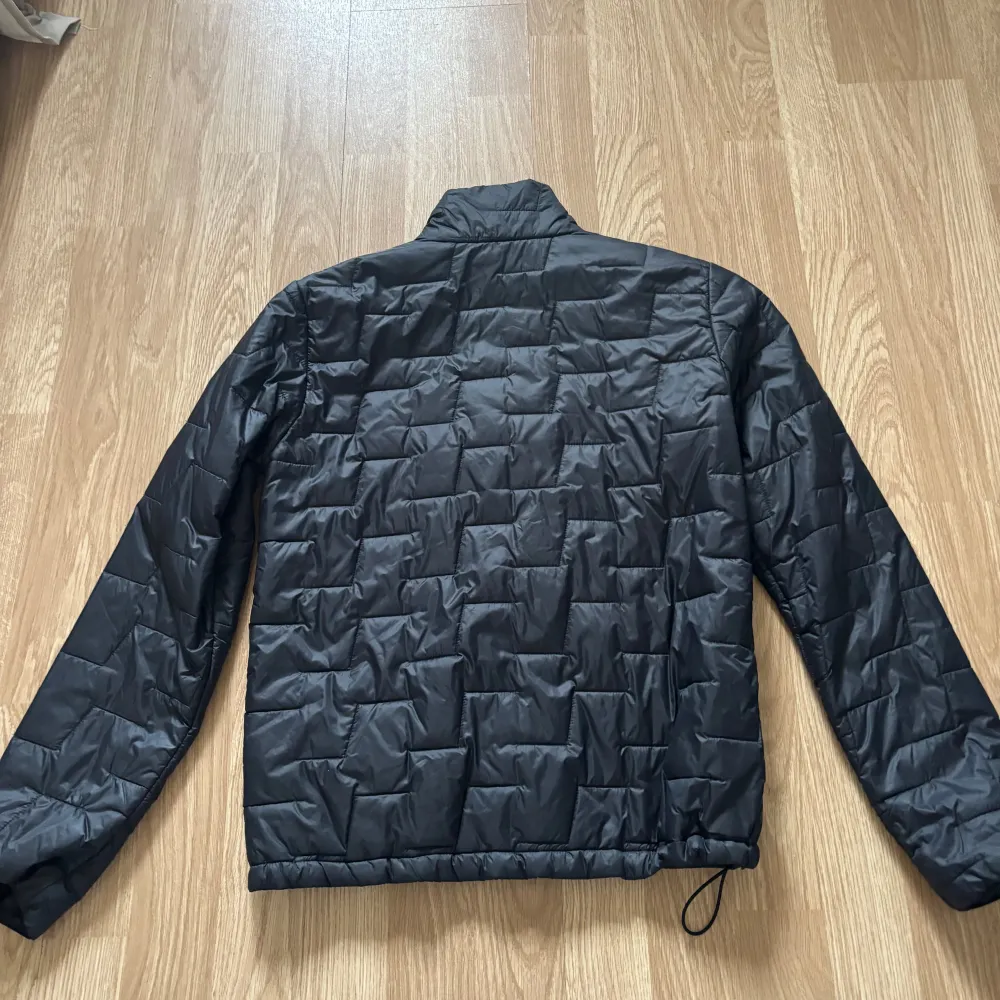 Snygg svart quiltad jacka från Helly Hansen med dragkedja framtill. Perfekt för kyligare dagar med sin stilrena design och bekväma passform. Jackan har långa ärmar och en diskret logga på bröstet.. Takit.