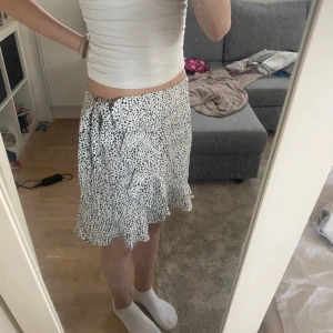 Vit-svart kjol - Kjolen är använd ganska många gånger men är i superskick! Den har inga skador eller fläckar utan den är som ny. Det är en volang rakt över kjolen och de är band som man knyter för att bestämma hur hårt den ska sitta i midjan. Jag skulle säga att den passar XS-M. Midjestorlek: 33-45cm. Längd: 40cm.