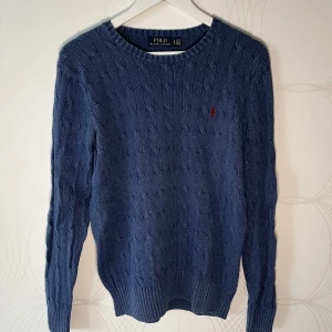 Ralph Lauren kabelstickad tröja - Ljusblå kabelstickad tröja från Ralph Lauren med röd broderad logga på bröstet. Använd men i bra skick. Storlek "S P" enligt märkning vilket står för Small Petite.    Hör av dig PM vid intresse!