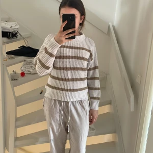 Vit och beige randig tröja - Säljer en vit och beige randig tröja med långa ärmar. Tröjan har en ribbad struktur och rund halsringning. Perfekt för en avslappnad stil. Passar bra till både jeans och mjukisbyxor.