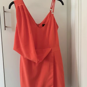 Orange one-shoulder jumpsuit  - Snygg orange one-shoulder jumpsuit med dubbel axelrem och dragkedja i ryggen. Perfekt för en somrig look med sin fräscha färg och stilrena design.