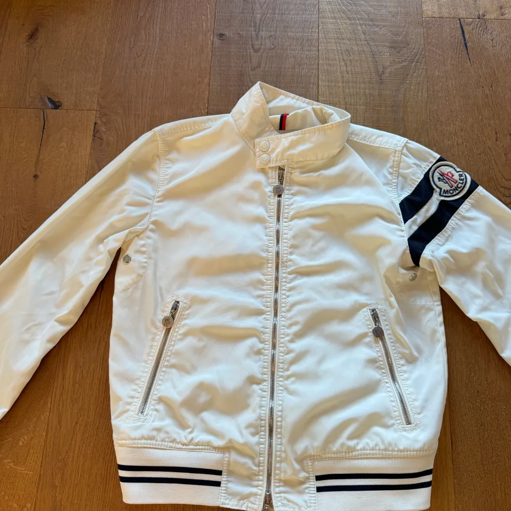 Säljer en stilren vit jacka från Moncler med dragkedja och ribbade detaljer. Jackan har ett broderat Moncler-märke på ärmen och två praktiska fickor med dragkedja. Perfekt för vår och höst! Storlek 1 passar S. Hör av er för frågor eller funderingar . Takit.