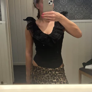 Body med volanger  - Snygg svart ärmlös topp med volangdetaljer vid axlarna. Perfekt för en kväll ute eller en speciell tillställning. Toppen har en elegant och stilren design som passar till många olika outfits.