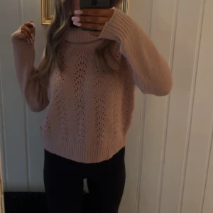 Rosa stickad polotröja - Mysig rosa stickad polotröja med ett fint hålmönster. Tröjan har långa ärmar och en bred polokrage som ger extra värme. Perfekt för kyliga dagar!