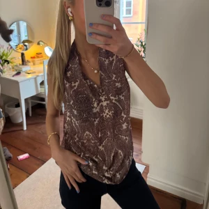 Mönstrad ärmlös blus - Snygg mönstrad ärmlös blus med v-ringning. Perfekt för en stilren look. Passar bra till både jeans och kjol.