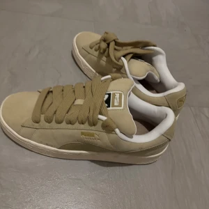Beige sneakers från Puma - Snygga beige sneakers från Puma i mocka med breda snören och vit sula. Perfekta för en avslappnad stil och bekväma att bära hela dagen.