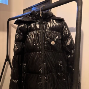 Svart dunjacka från Moncler - Snygg svart dunjacka från Moncler med glansig finish. Jackan har en dragkedja framtill och en hög krage för extra värme. Perfekt för kyliga dagar. Från 🇨🇳för dom som förstår fast en väldigt bra