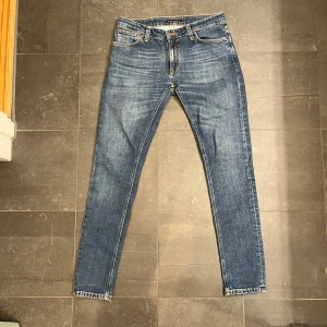 Blå jeans från Nudie Jeans - Snygga blå jeans från Nudie Jeans med klassisk femficksdesign och orange sömmar. De har en normal passform och är tillverkade i slitstarkt denim. Perfekta för en avslappnad stil.