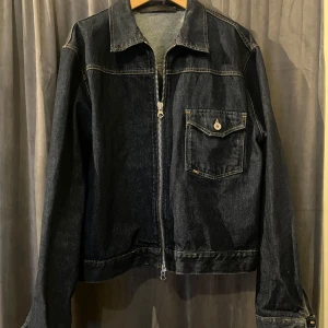 Blå cropped jeansjacka med dragkedja - Snygg blå jeansjacka med dragkedja och en bröstficka med knapp. Perfekt för en casual look.