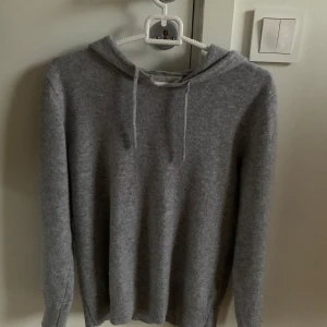Grå hoodie i kashmir - Säljer en stilren och mjuk grå hoodie i kashmir. Perfekt för kyliga dagar med sin bekväma passform och klassiska design. Den har en justerbar huva med snören och ribbade muddar vid ärmslut och nederkant. Fin Kashmir hoddie från märket Sayless. Otroligt bra passform. Nypris 899. Den är lite sönderdragen upptill där snörerna sitter. 