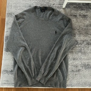 Grå tröja från Polo Ralph Lauren - Säljer en stilren grå tröja från Polo Ralph Lauren med deras ikoniska logga broderad på bröstet. Tröjan har långa ärmar och är tillverkad i mjuk bomull. Perfekt för en avslappnad och snygg look.