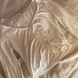 Vit långärmad topp med rynkdetalj - En vit långärmad topp med v-ringning och snygg rynkdetalj framtill. I storlek M från Nelly. 