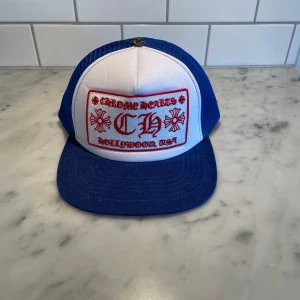 Blå och vit keps från Chrome Hearts - Snygg keps från Chrome Hearts i blått och vitt med broderad text och motiv på framsidan. Kepsen har ett nätmaterial på baksidan. Pris kan diskuteras!